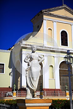 Trinidad City, Cuba. Female statue in the Plaza Mayor against the background of the Church of the Holy Trinity