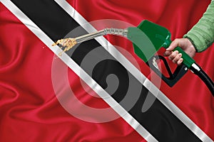 TRINIDAD AND TOBAGO flag Close-up shot on waving background texture with Fuel pump nozzle in hand. The concept of design solutions