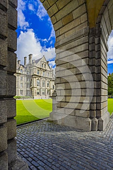 Trinity College Dublin, Ireland. The image features a view of the college through a stone archway, with cobblestones and trees in photo