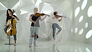 Trio girls playing the violins one on the cello in the white studio