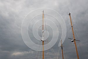 Trio of ship masts, rigging but no sails, against threatening skies with storm clouds