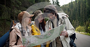 A trio of tourists get lost and are looking at a map to figure out where to go next. People in hiking clothes sort out