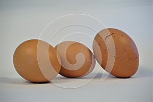 Three brown eggs on white background, one cracked photo