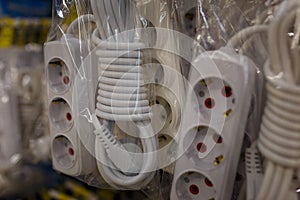 A triple socket extension cord, joint with three rosettes and white electrical cable in plastic package in tools store, shop or