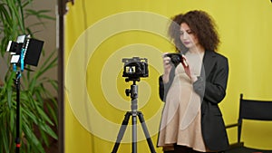 Tripod with camera and light stand with blurred pregnant woman talking filming blog at yellow background. Young