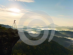 Tripod with camera on view point ready for photography. Exposed rocky edge above landscape.