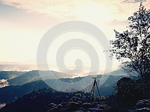 Tripod with camera on view point ready for photography. Exposed rocky edge above landscape.