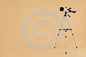 Tripod with modern telescope on beige background, space for text