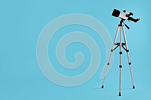 Tripod with modern telescope on light blue background, space for text