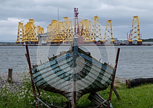 Tripods for supporting wind turbines awaiting relocation, photographed in Cromarty, Scotland, with old blue boat in foreground.