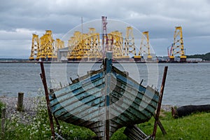 Tripods for supporting wind turbines awaiting relocation, photographed in Cromarty, Scotland, with old blue boat in foreground.