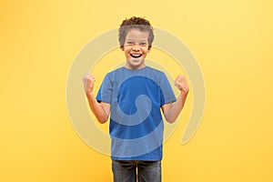 Triumphant boy with fists pumped in blue shirt, yellow background