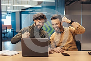 Triumphant coworkers celebrating business achievement or success, making great deal, looking at laptop screen at office