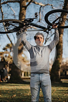 Triumphant young man lifting bicycle overhead in a park setting