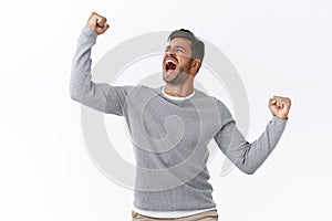 Triumphing young hispanic guy feeling like champion of world, celebrating success or win, yelling yes as finish