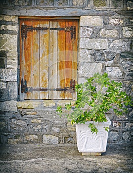 Old wooden window shutters on stone wall and a flowerpot