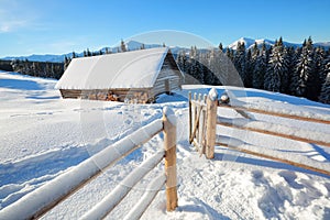 A trodden path leads to the wooden house in the snow on the background of beautiful snow capped mountains.