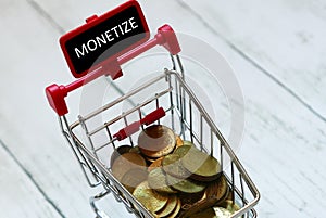 Trolley or shopping cart and gold coins with blackboard written with word monetize.Business and finance concept.