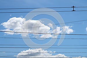 Trolleybus wires against the background of white clouds and blue sky, urban public transport.