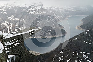 Trolltunga cliff under snow in Norway. Scenic Landscape. Man traveller sitting on edge of rock in yoga meditation pose