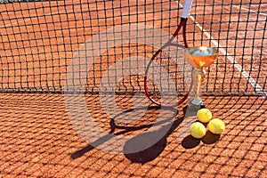 Trophy, professional tennis racket and balls on a red clay tennis court and net shadow. Winning concept. Copy space