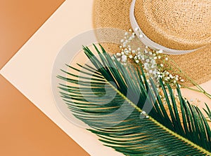 Tropic leaves, straw hat on brown background. Trendy fashion accessories. Flat lay, close up. Summer, vacation, holidays concept.