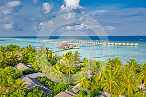 Tropical aerial island paradise with white sandy beach shore, seaside summer palm trees with sea horizon and luxury water villas