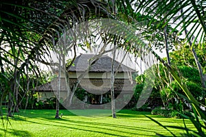 Tropical authentic hotel surrounded by palm greenery stands on the lawn.