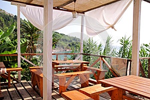 Tropical beach cafe bar at coastline by sea with outdoor view. Terrace balcony, relax place for eating and drinks of seaside.