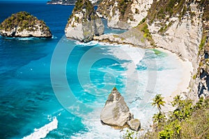 Tropical beach with coconut palms and rock in Nusa Penida, Bali