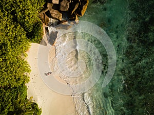 Tropical beach, coral sand, green vegetation, large rocks, waving ocean, splashes, and a red swisuit sexy woman from high above, b