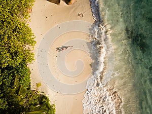 Tropical beach, coral sand, green vegetation, large rocks, waving ocean, splashes, and a red swisuit sexy woman from high above, b