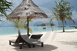 Tropical beach with deckchairs, umbrellas, boats and palm trees