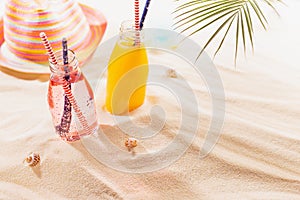 Tropical beach fruit cold strawberry and orange cocktail in glass bottle with straw, sun hat, toy under green palm leaf in sun.