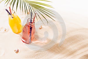 Tropical beach fruit cold strawberry and orange cocktail in glass bottle with straw under green palm leaf in sun beam with shadows