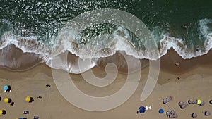 Tropical beach with green sea and sunbathers with colorful umbrellas. Drone in vertical and moves until the sea occupies the entir