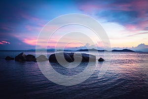 Tropical beach holidays landscape with calm turquoise sea and big round stones and rocks in sea during dramatic sunset in purple c