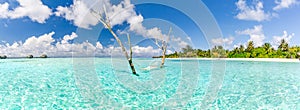 Tropical beach panorama as summer landscape with beach swing or hammock and white sand and calm sea for beach banner