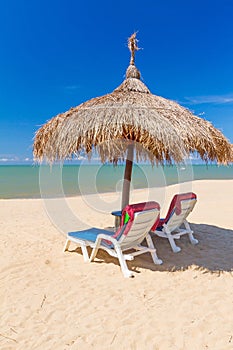 Tropical beach scenery with parasol and deck chairs