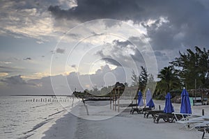 Tropical beach in sunrise with overcast, sun beds and blue sun shades