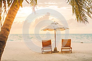 Tropical beach sunset, romantic landscape with two chairs and umbrella near the sea with palm trees.