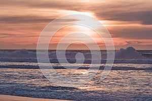 Tropical beach sunset in soft blue and pink colors. Empty sand beach, huge waves, and beautiful cloudy sky