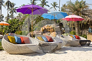 Tropical beach with swimming pool, coconuts palm trees, rattan daybeds and umbrella near sea, Thailand