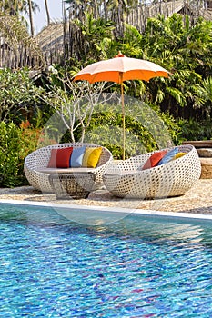 Tropical beach with swimming pool, coconuts palm trees, rattan daybeds and umbrella near sea, Thailand