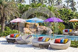 Tropical beach with swimming pool, coconuts palm trees, rattan daybeds and umbrella near sea, Thailand