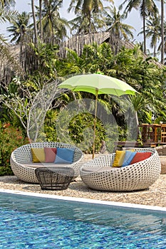 Tropical beach with swimming pool, coconuts palm trees, rattan daybeds and umbrella near sea, Thailand