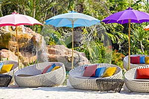 Tropical beach with swimming pool, coconuts palm trees, rattan daybeds and umbrella near sea, Thailand