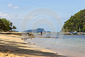 Tropical beach with trees, boats and isles on horizon. Seascape with tourist on beach. Tropic paradise.