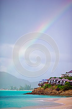 Tropical beach with turquoise water in the ocean, white sand and colorful rainbow over the sea