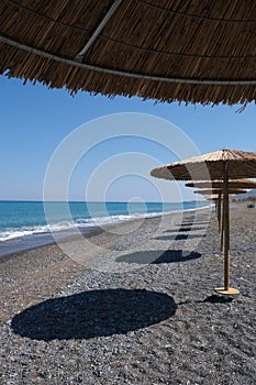 Tropical beach umbrellas providing sunshade for swimmers at an empty beach. Summer vacations.